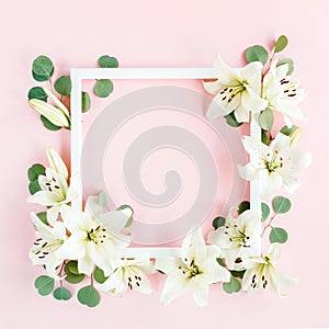 Floral frame made of white lilies and eucalyptus leaves on pink background. Flat lay, top view floral mockup with empty