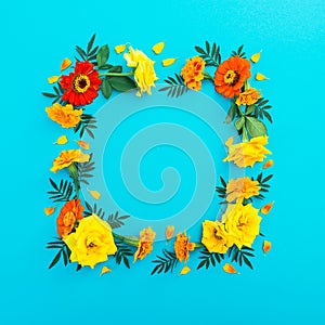 Floral frame made of yellow and red flowers with petals on blue background. Flat lay, top view. Floral background.