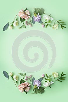 Floral frame with pink roses, white flowers, branches, leaves and petals on green background. Flat lay, top view
