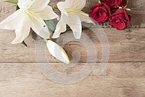 Floral frame with stunning white lilies and red roses on wooden background. Copy space. Wedding, gift card, valentine's day