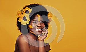 Floral gracefulness. Studio shot of a beautiful young woman smiling while posing with sunflowers in her hair against a