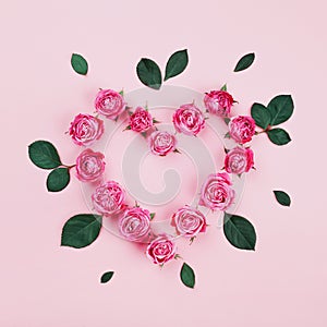 Floral heart made of pink rose flowers and green leaves on pastel background top view. Flat lay styling. Fashion composition.