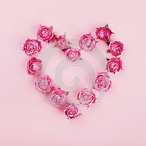 Floral heart made of pink rose flowers on pastel background top view. Flat lay styling. Fashion and creative composition.