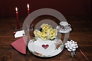 Floral pattern fine china dinnerware with matching plate, cup and saucer. bouquet of yellow roses, pink napkin, silverware, red ca