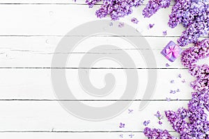 Floral pattern of lilac branches, petal and pink box for rungs on wooden background. Flat lay, top view.