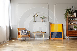 Floral print on an orange upholstered armchair in an elegant living room interior with hardwood floor and place for a sofa. Real p photo