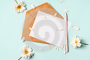 Floral romantic composition. White chamomile flowers and an envelope on a pastel blue background with petals. Valentine`s Day, Ea