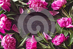 Floral vintage frame of pink peonies with leaves and petals on wooden background
