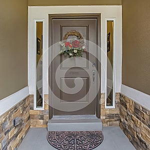 Floral wreath hanging on the gray front door of a house with sidelights