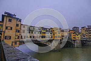 Florence, Italy: View on the Florence Ponte Vecchio with colorful stores on a rainy day across river Arno and dramatic gray sky