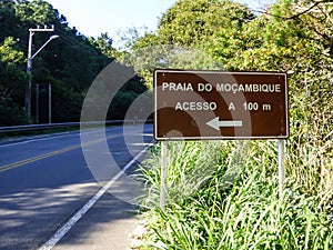 Sign by the road reading `Mocambique beach, access in 100 meters`. Mocambique is the longest beach in the island of Florianopolis