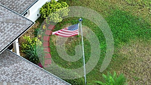 Florida suburban home with USA national flag waving on wind in front yard. American stars and stripes spangled banner as
