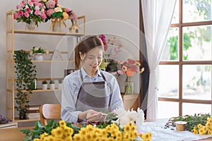 Florist concept, Woman florist making white chrysanthemum bouquet and tie ribbon at flower shop