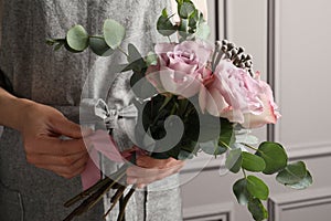 Florist creating beautiful bouquet at white wall, closeup