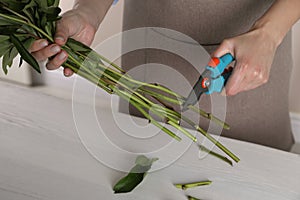 Florist cutting stems of flowers with pruner at workplace, closeup