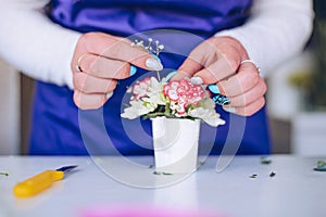 The florist hands creates a composition of flowers in a small white pot. photo