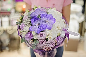 Florist holding tender flower composition in blue, white and purple tones consisting of roses and other beautiful flowers