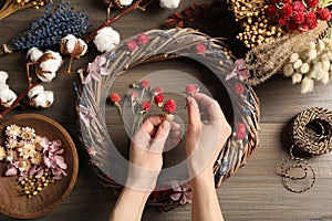 Florist making wreath with dried flowers at wooden table, top view