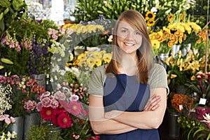 Florist Standing In Shop In Front Of Flower Display