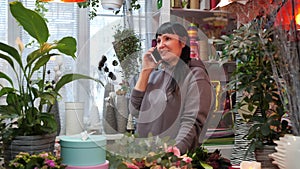 Florist talking by mobile phone in flower studio. Female seller in flower shop talking with client by telephone.