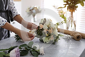 Florist tieing bow of beautiful wedding bouquet at light grey marble table, closeup