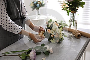 Florist tieing bow of beautiful wedding bouquet at light grey marble table, closeup