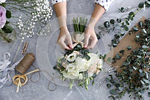 Florist tieing bow on beautiful wedding bouquet at light grey marble table, top view