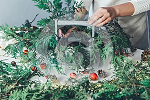 Florist woman makes Christmas composition for table decoration from thuja, spruce branches in wooden box. Using of floral foam,