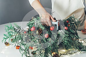 Florist woman makes Christmas composition for table decoration from thuja, spruce branches in wooden box. Using of floral foam,