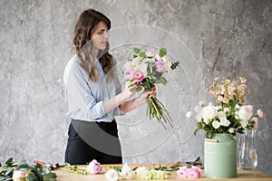 Florist at work: pretty young woman making fashion modern bouquet of different flowers