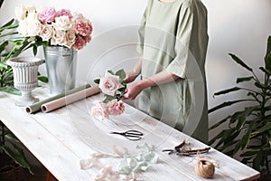 Florist at work: a woman shows an assembly of a bouquet of roses and carnations. Florist`s workplace in a light space. Florist at