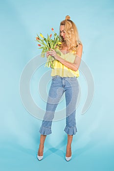 Floristics, holidays and people concept - Beautiful blonde young woman holding bunch of tulips on blue background