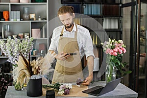 Florists making bouquet of flowers on counter and taking photo on smartphone for social media.