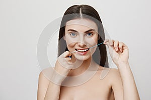 Floss is important for tooth care. Indoor shot of attractive european woman with blue eyes flossing teeth, trying to