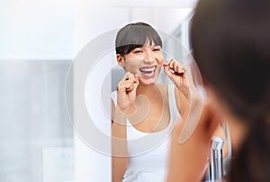 Flossing away. Shot of a cheerful attractive young woman flossing her teeth while looking at her reflexion in a mirror