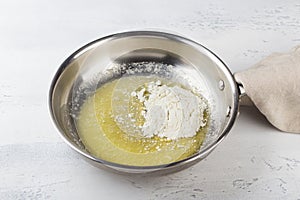 Flour is added to melted butter in a frying pan on a light gray background. Making cheese pasta sauce, step by step, do