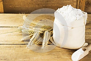 Flour in bag and wheat ears on a wooden background. Copy space.