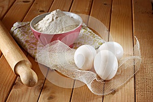Flour in bowl with eggs and rolling pin over wood table