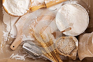 Flour in a bowl and wheat grains with wheat ears on the table, paper background In a rustic kitchen, top view