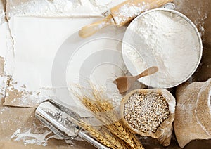 Flour in a bowl and wheat grains with wheat ears on the table, paper background In a rustic kitchen, top view