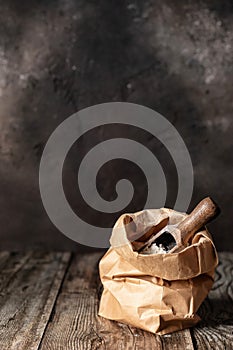 Flour in brown craft paper bag on dark wooden background, rustic style, copy space