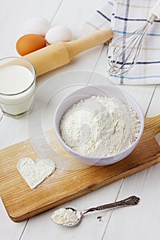 Flour in ceramic bowl with eggs, milk and heart from a flour