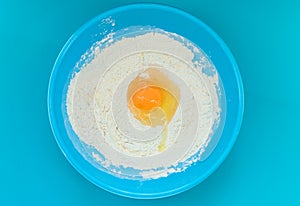 Flour and egg in a blue bowl on a blue background. Top view.