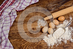 Flour, eggs, salt, towel, rolling pin on wooden table ready for cooking