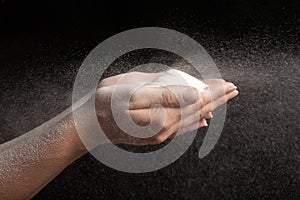 Flour in hands blowing on black background like snow