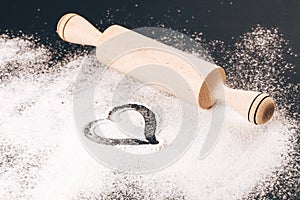 Flour with heart and rolling pin on black