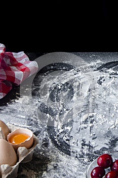 Flour and ingredients for sweet berry pie lie on the black table