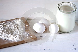 Flour, milk and eggs on a wooden white table