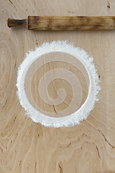 Flour powder sprinkled in a circle on cutting board and wooden table background