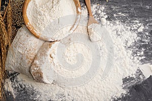 Flour in a sack and wheat flour in a wooden bowl There are ears of wheat on the table on, black background - Top view